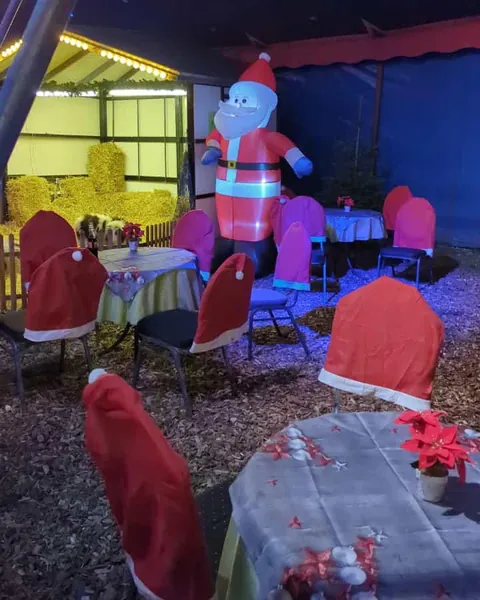 Gedeckte Tische mit Weihnachtssternen und Stühlen in Nikolausmützen, dahinter ein großer Weihnachtsmann