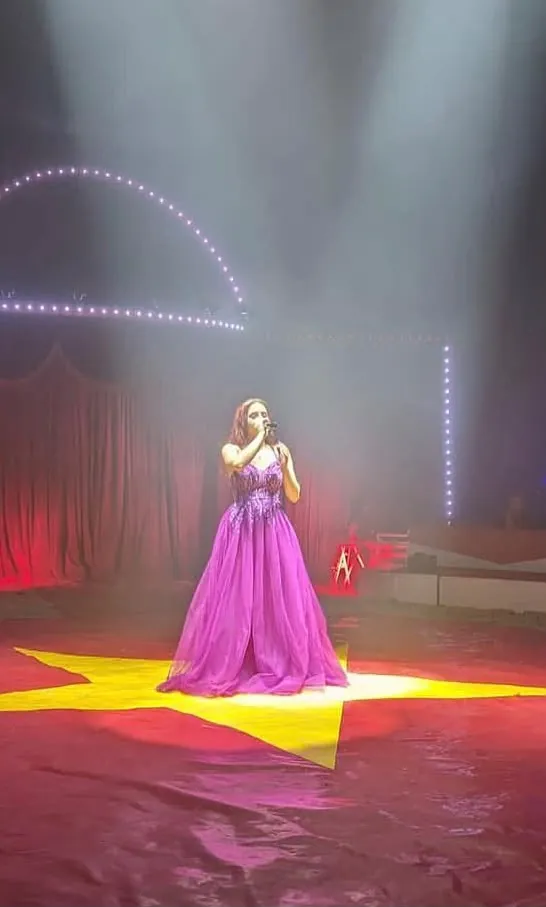 Sängerin im pinken Abendkleid mit Mikrofon auf einem gelben Stern in der Manege